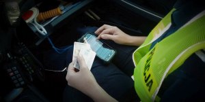 Policjantka siedzi wewnątrz radiowozu. Na urządzeniu mobilnym sprawdza dokumenty zatrzymanej do kontroli osoby.
